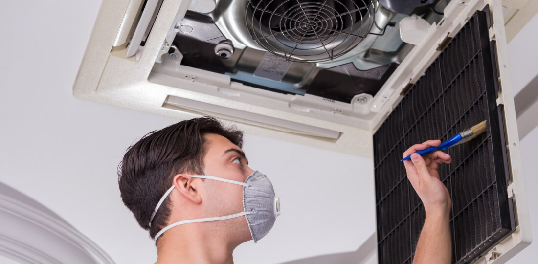 Person in face mask using a brush to clean an air filter